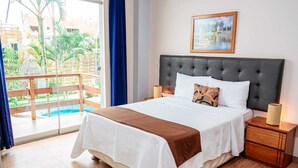 A hotel room with a bed, nightstands, a painting, and a view of a pool and greenery. - Gran Hotel Villa Del Sur (San Vicente de Cañete)