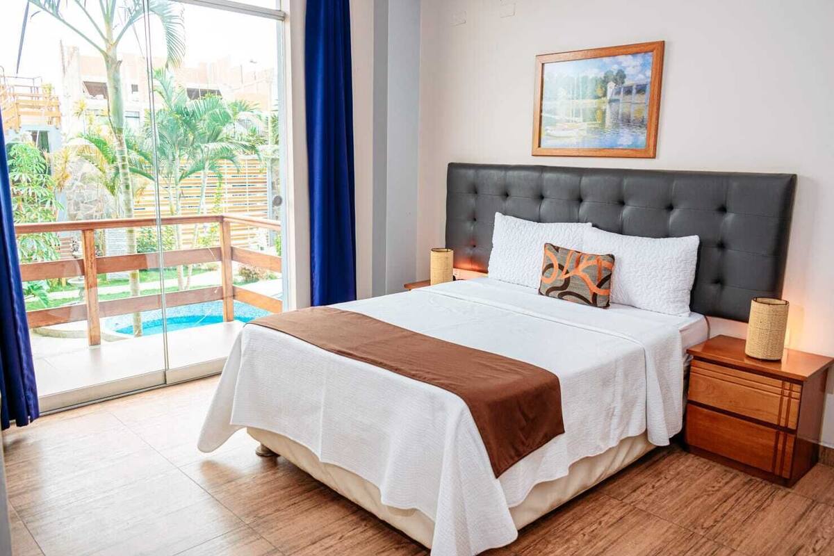 Ein Hotelzimmer mit Bett, Nachttischen, einem Gemälde und Blick auf Pool und Grünflächen.