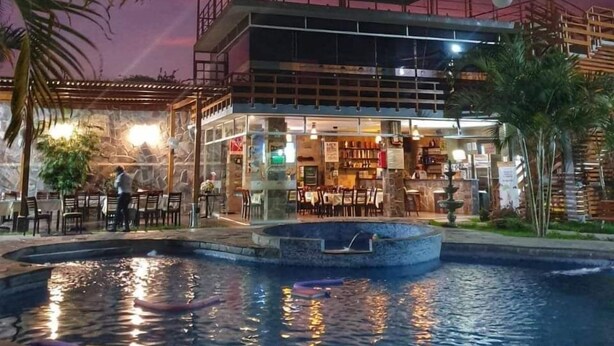 A restaurant with outdoor seating, a pool, and a stone wall backdrop. - Gran Hotel Villa Del Sur (San Vicente de Cañete)