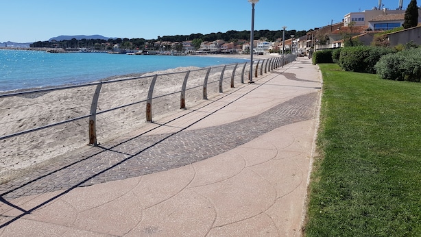 Eine Uferpromenade mit gepflastertem Weg, Metallgeländer und einer Rasenfläche.