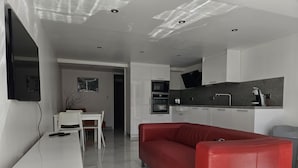 Eine moderne Küche mit weißen Schränken, einem roten Sofa und einem Essbereich mit weißem Tisch und Stühlen.