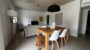 Ein moderner, gut beleuchteter Raum mit einem Holzesstisch, weißen Stühlen, einer Bank und einer großen schwarzen Pendelleuchte.