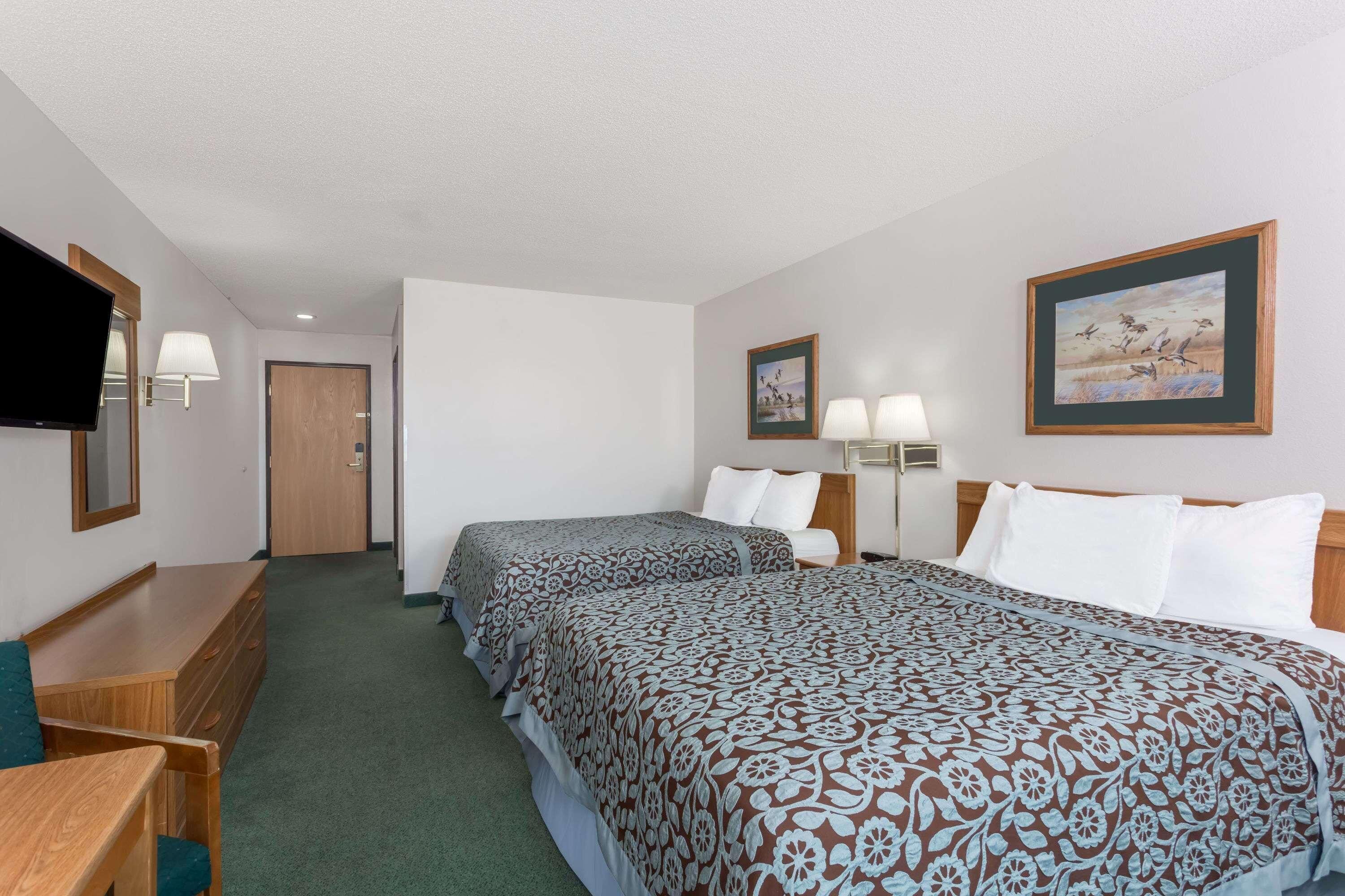 A hotel room with two beds, a desk, a chair, a TV, and a door.