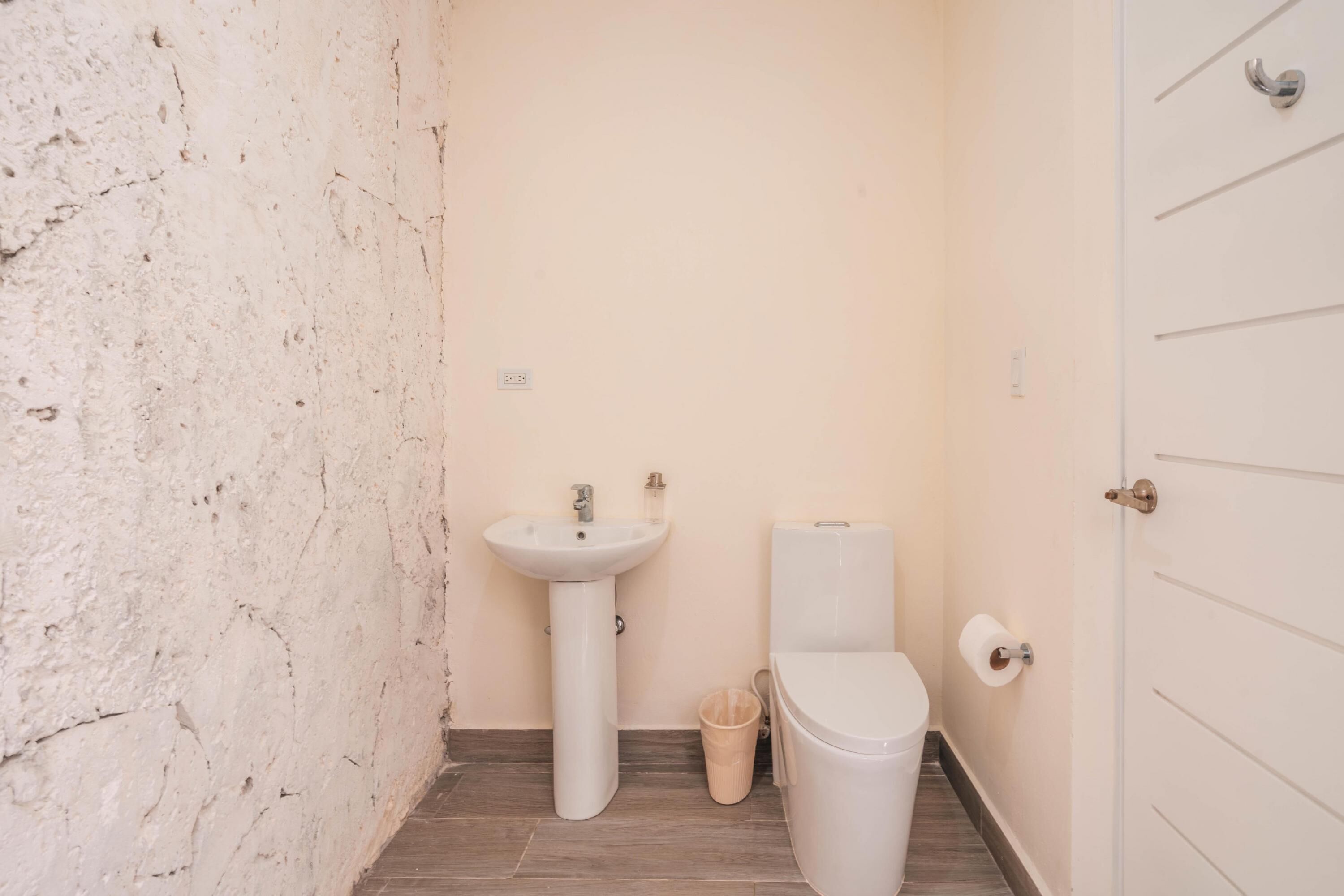 A small bathroom with a white sink, toilet, and a trash bin.