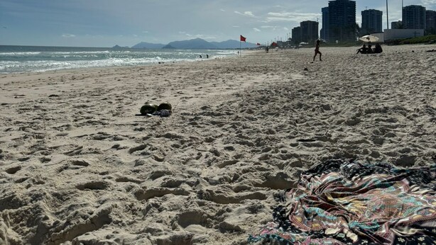 A sandy beach with footprints, a colorful blanket, and buildings in the background.