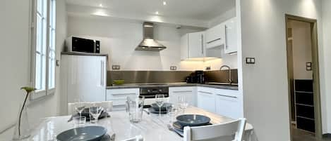 A modern kitchen with white cabinetry, a central island, and a dining area set for four.