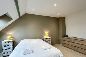 Quarto com cama, duas mesas de cabeceira com luminárias, cômoda de madeira e teto inclinado.