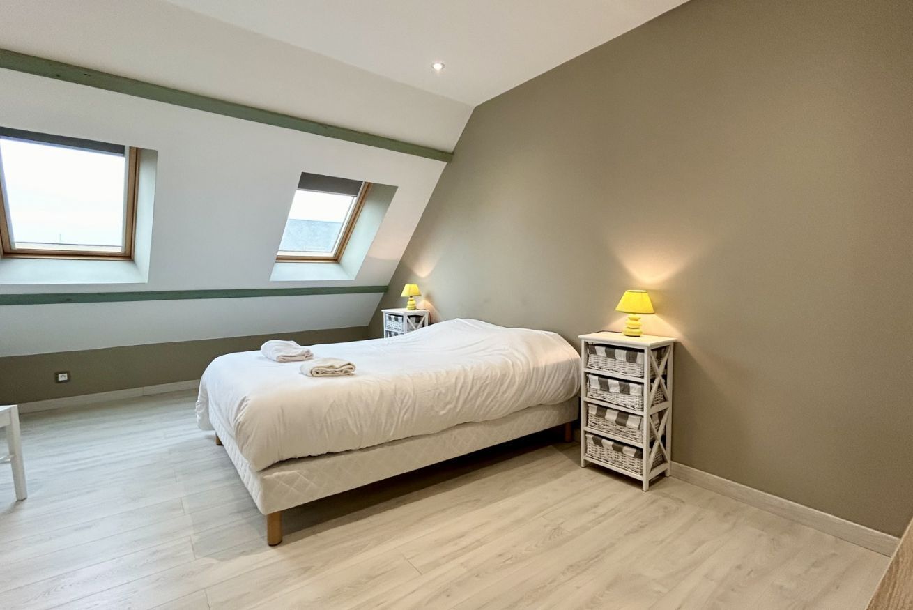 Une chambre à coucher avec un lit, deux tables de chevet avec des lampes, une chaise blanche et une lucarne.