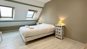 A bedroom with a bed, two bedside tables with lamps, a white chair, and a skylight.