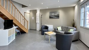 A modern living room with a staircase, a grey sofa, a television on a cabinet, and a painting on the wall.