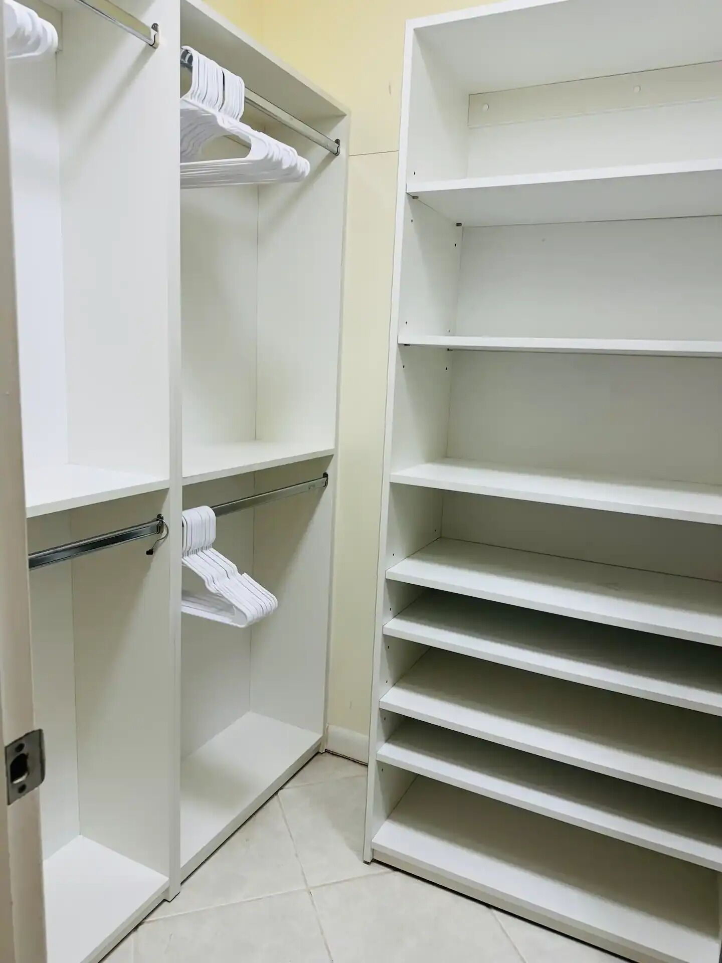 Ein weißer Kleiderschrank mit mehreren Regalen und Ablageflächen, ausgestattet mit Metallstangen und Haken zur Aufbewahrung.