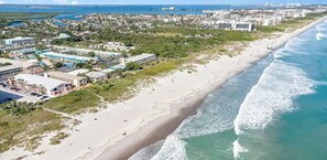 Vue aérienne d’une zone côtière avec une plage, des bâtiments et un port de plaisance.