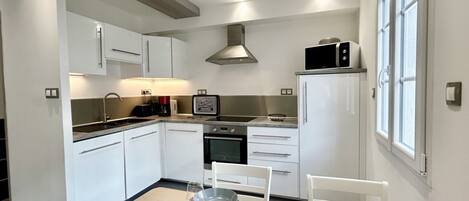 A modern kitchen with white cabinets, a stainless steel range hood, and a dining area with a table set for four.