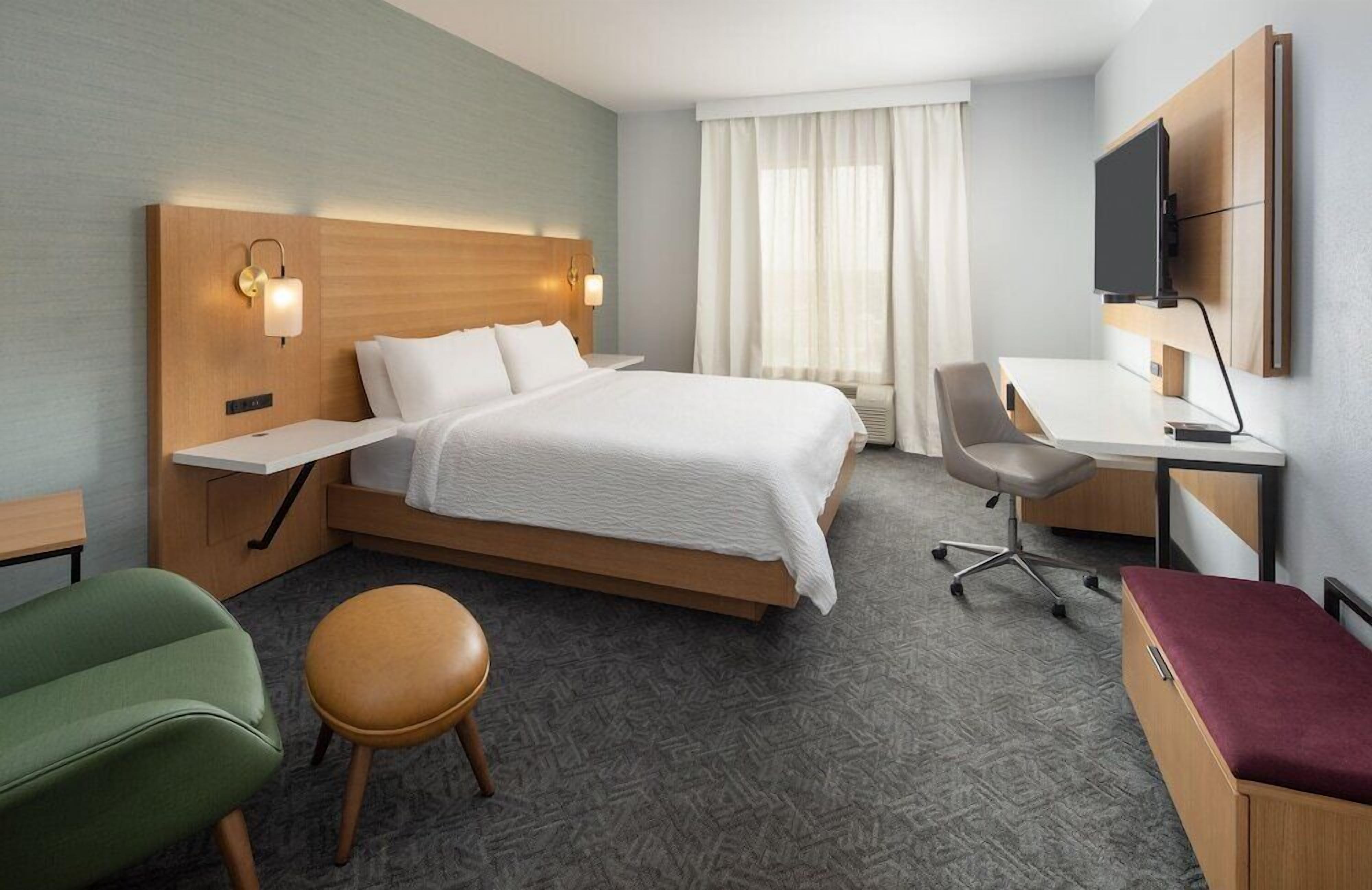 Habitación de hotel con cama, escritorio, silla y televisor.