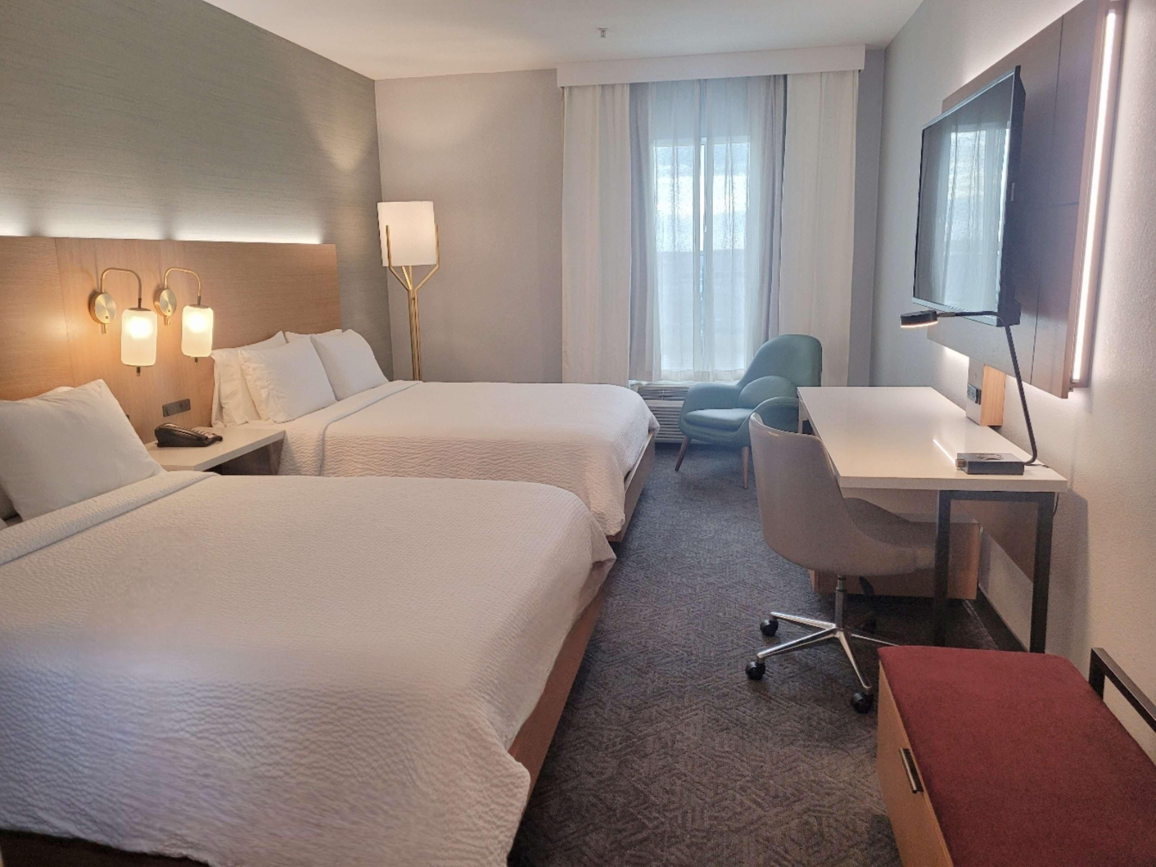 Une chambre d’hôtel avec deux lits, un bureau, une chaise, une télévision et une fenêtre avec des rideaux.