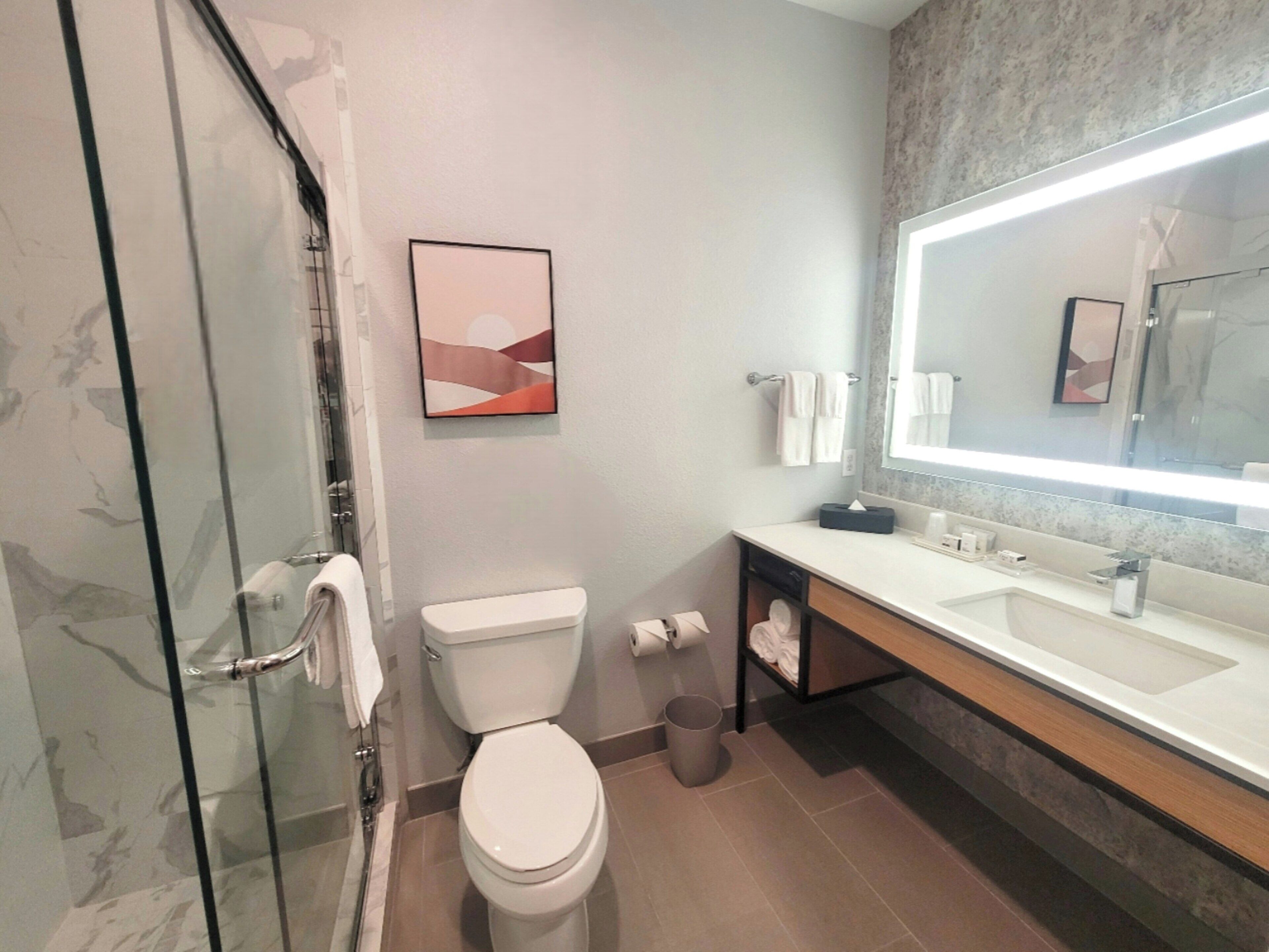 Un baño moderno con cabina de ducha de vidrio, inodoro, lavamanos con espejo y barra para toallas.