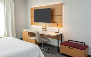 Ein Hotelzimmer mit Bett, Schreibtisch mit Stuhl, Wand-Fernseher und einem kleinen Schrank.