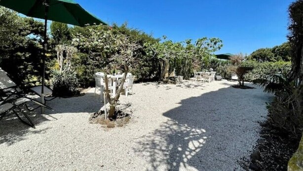 Une cour recouverte de gravier, avec un parasol vert, des chaises en pierre et diverses plantes.