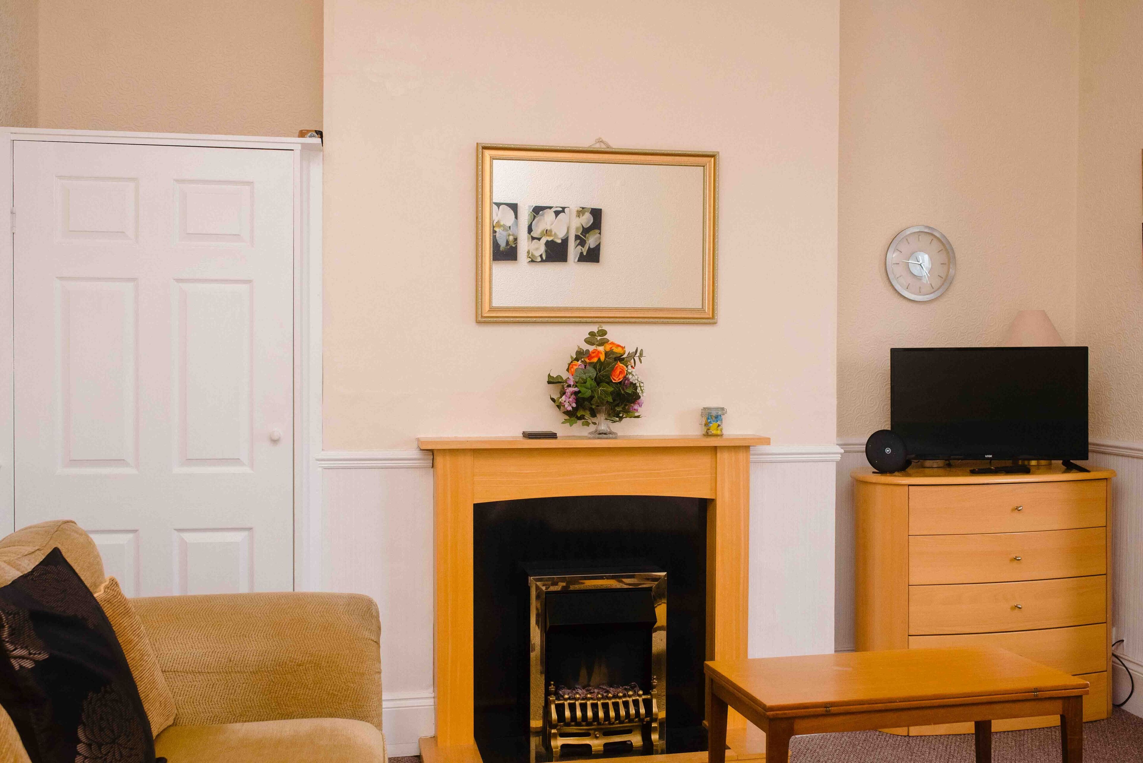 A living room with a fireplace, a television on a wooden cabinet, a door, and a framed picture on the wall.