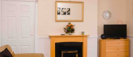 A living room with a fireplace, a television on a wooden cabinet, a door, and a framed picture on the wall.