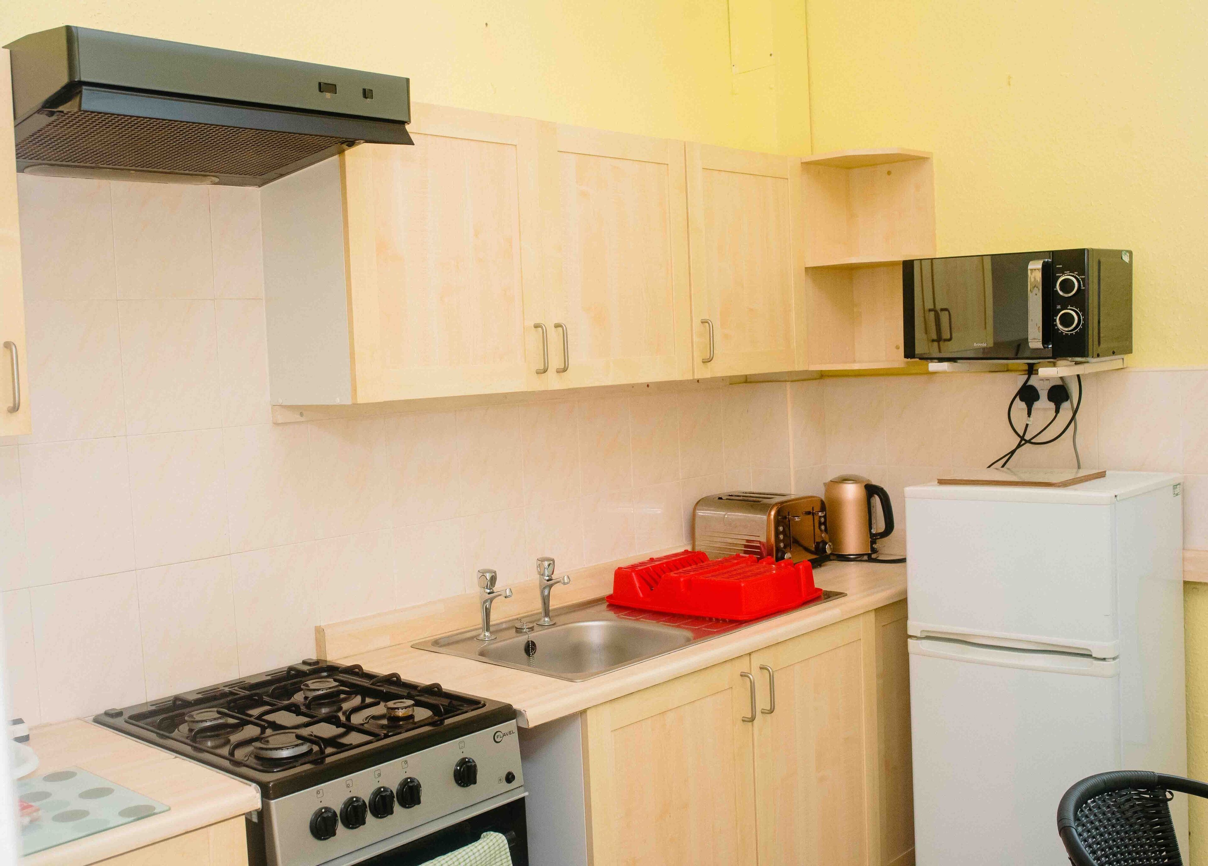 A compact kitchen with a gas stove, a sink, a toaster, a kettle, and a refrigerator.