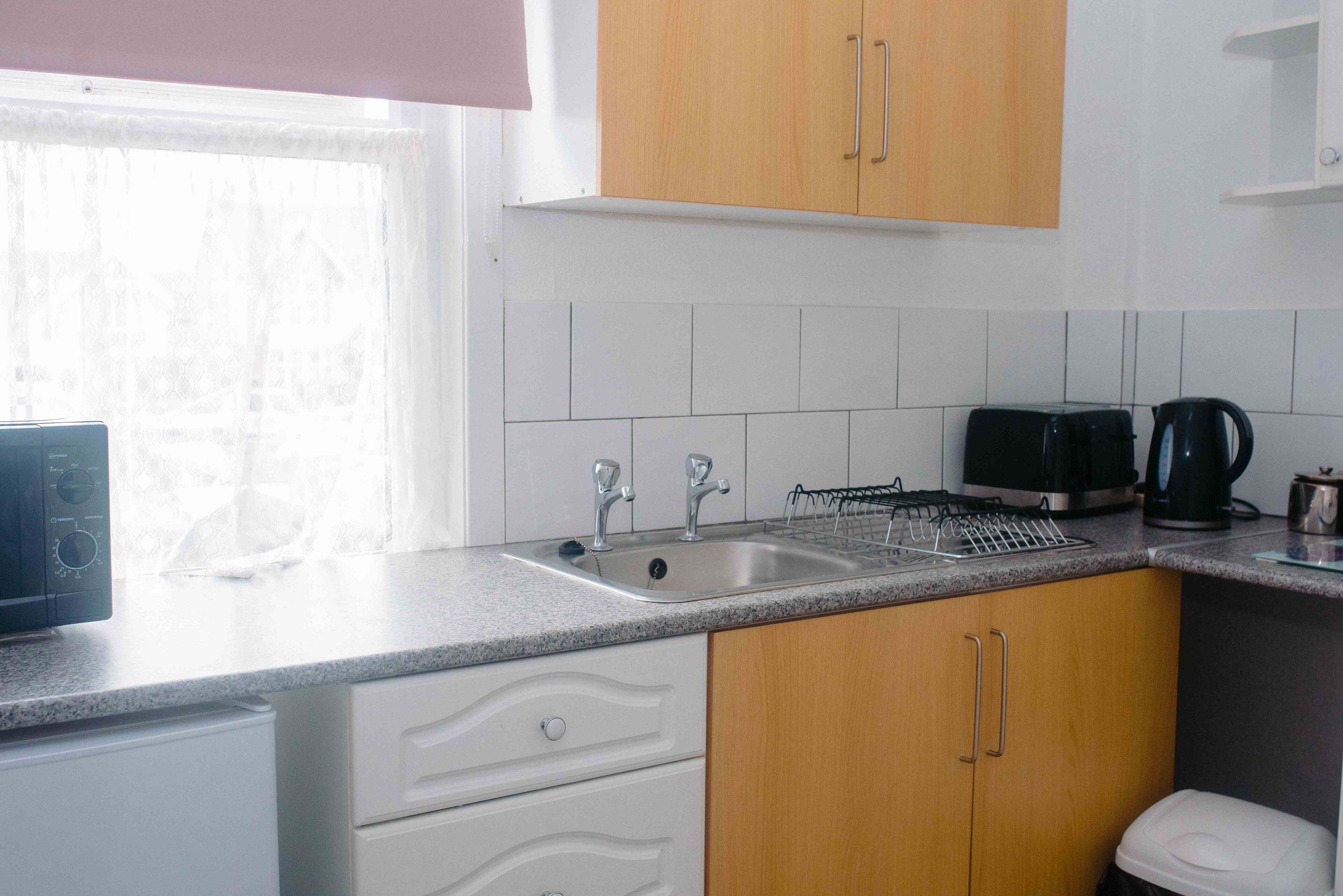 Uma cozinha com armários brancos, uma pia dupla, uma torradeira e uma chaleira.