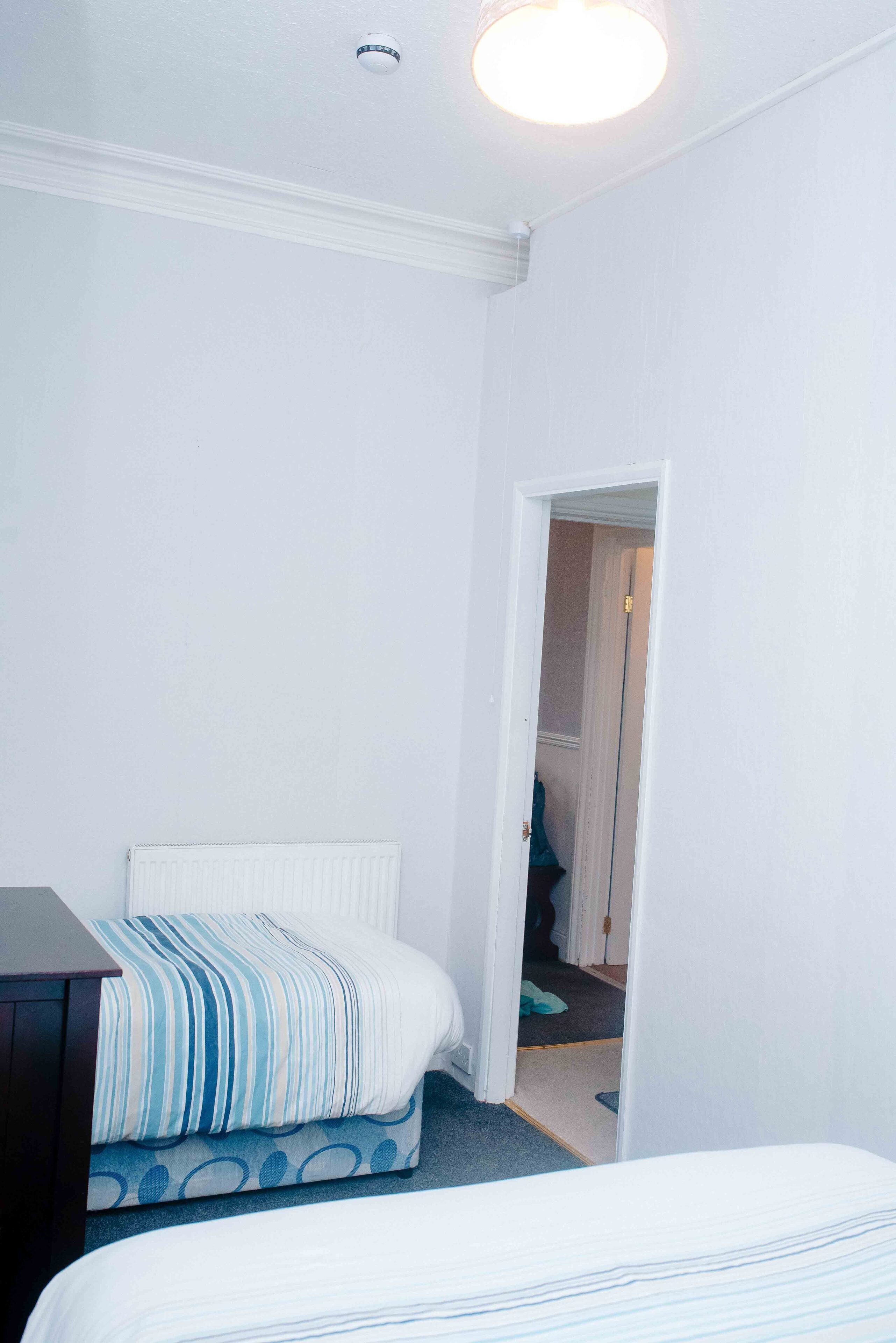 A bedroom with a bed, a radiator, and a door leading to another room.