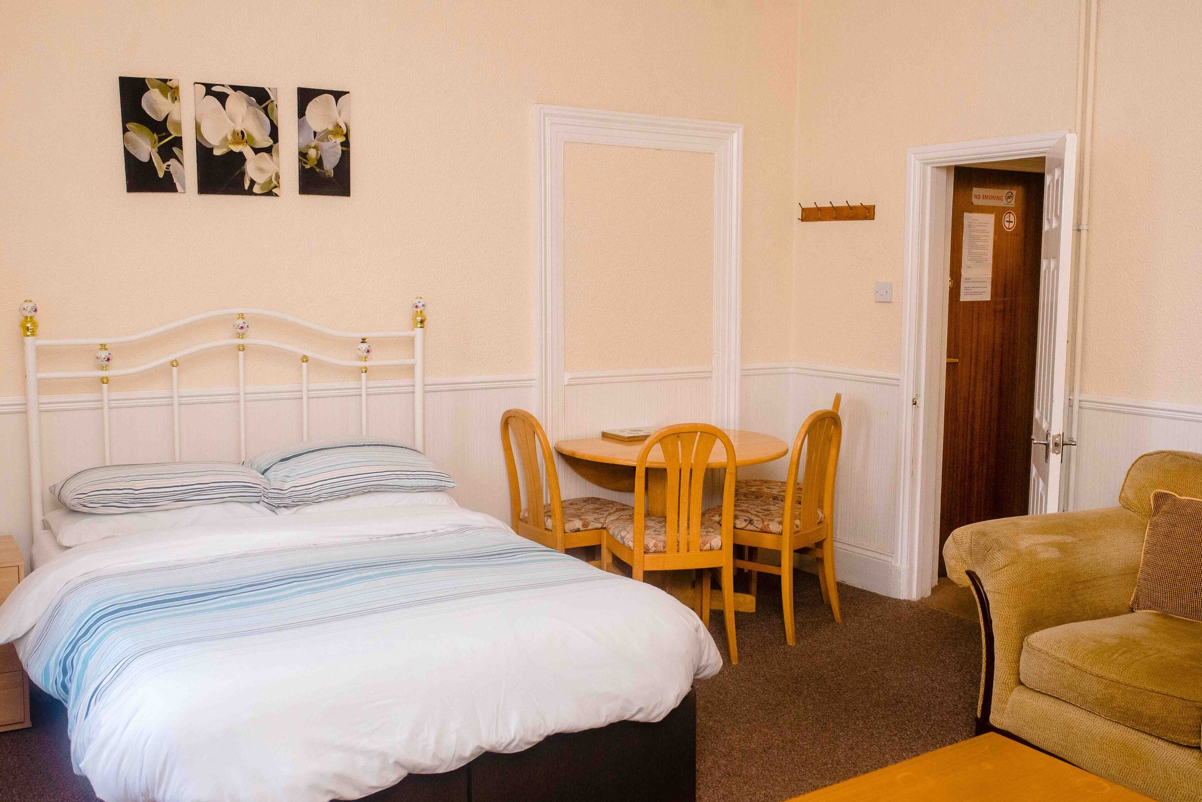 A bedroom with a bed, a round table with chairs, a sofa, and a door with a sign.