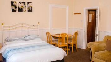 A bedroom with a bed, a round table with chairs, a sofa, and a door with a sign.