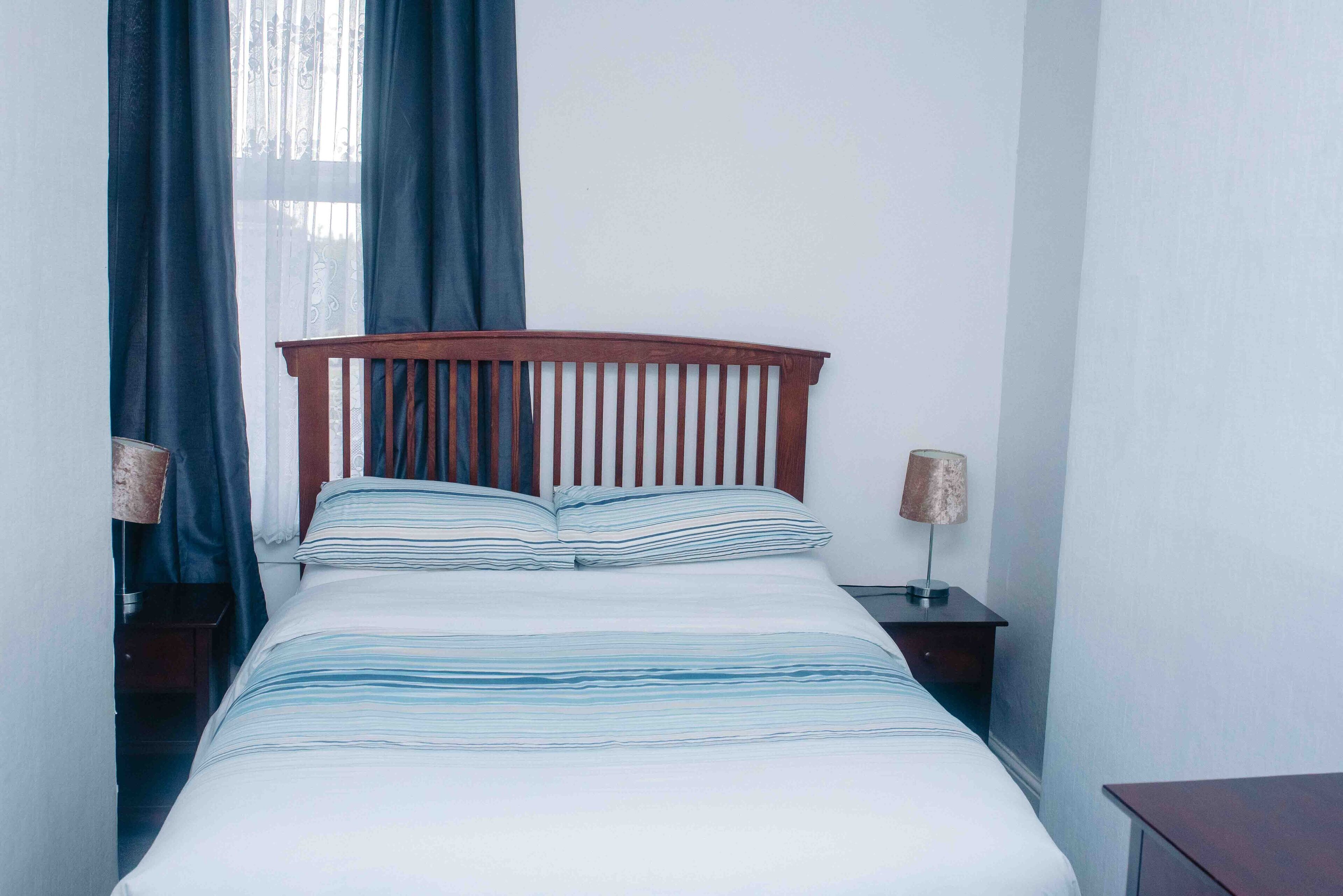 A neatly made bed with striped bedding, a wooden headboard, and two bedside lamps.