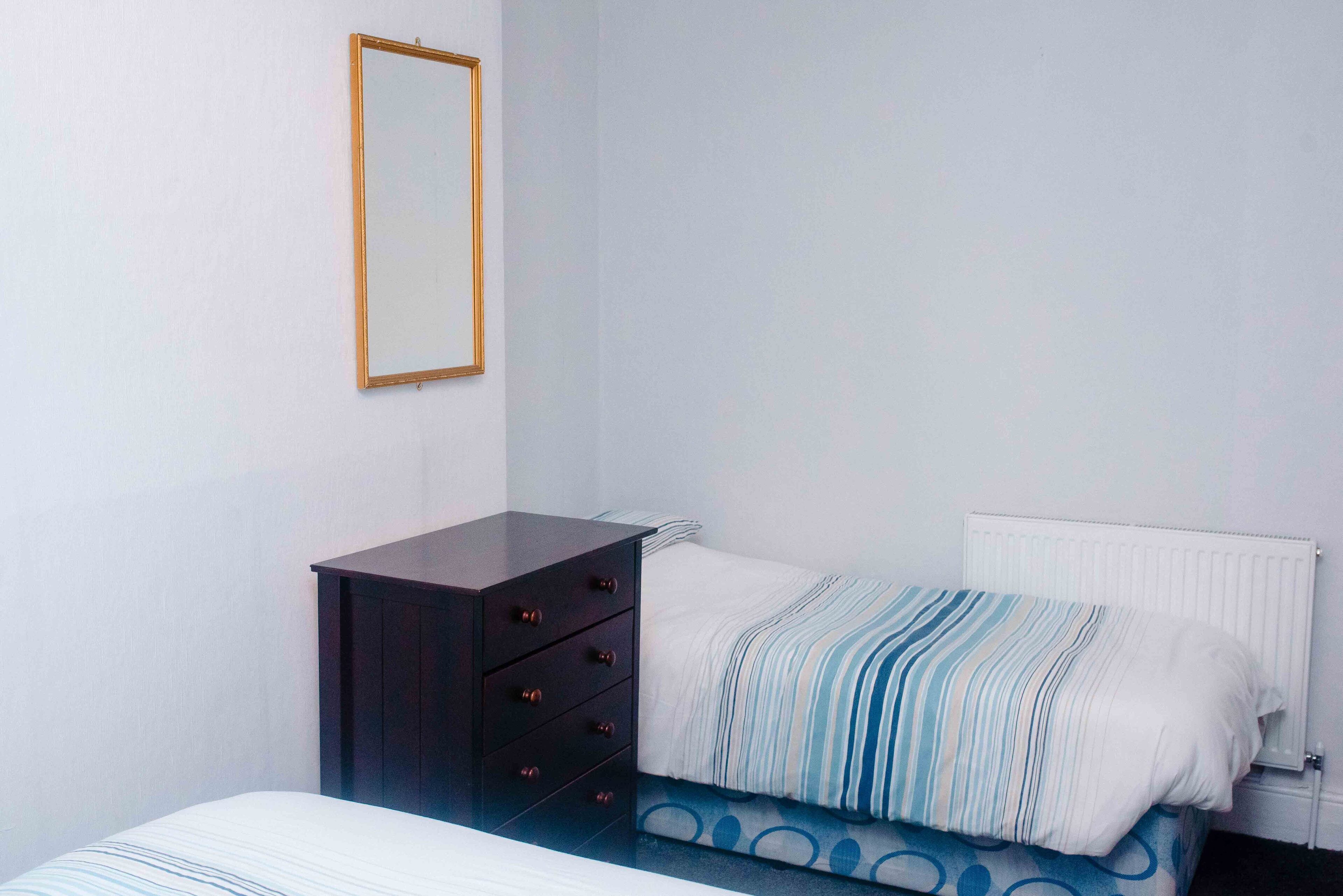 Ein Schlafzimmer mit Bett, Kommode, Heizkörper und Spiegel an der Wand.