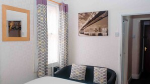 Habitación de hotel con cama, un cuadro colgado en la pared, cortinas y una puerta que da a otra habitación.