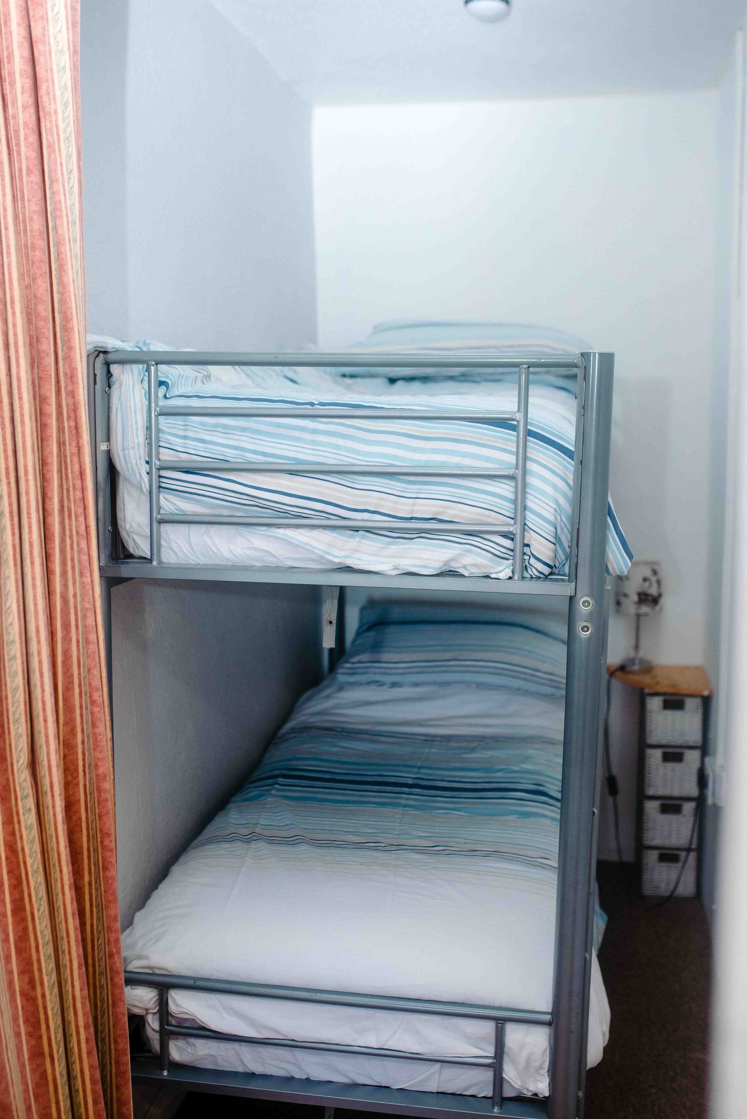 A bunk bed with striped bedding in a room with a wooden nightstand and a power outlet.
