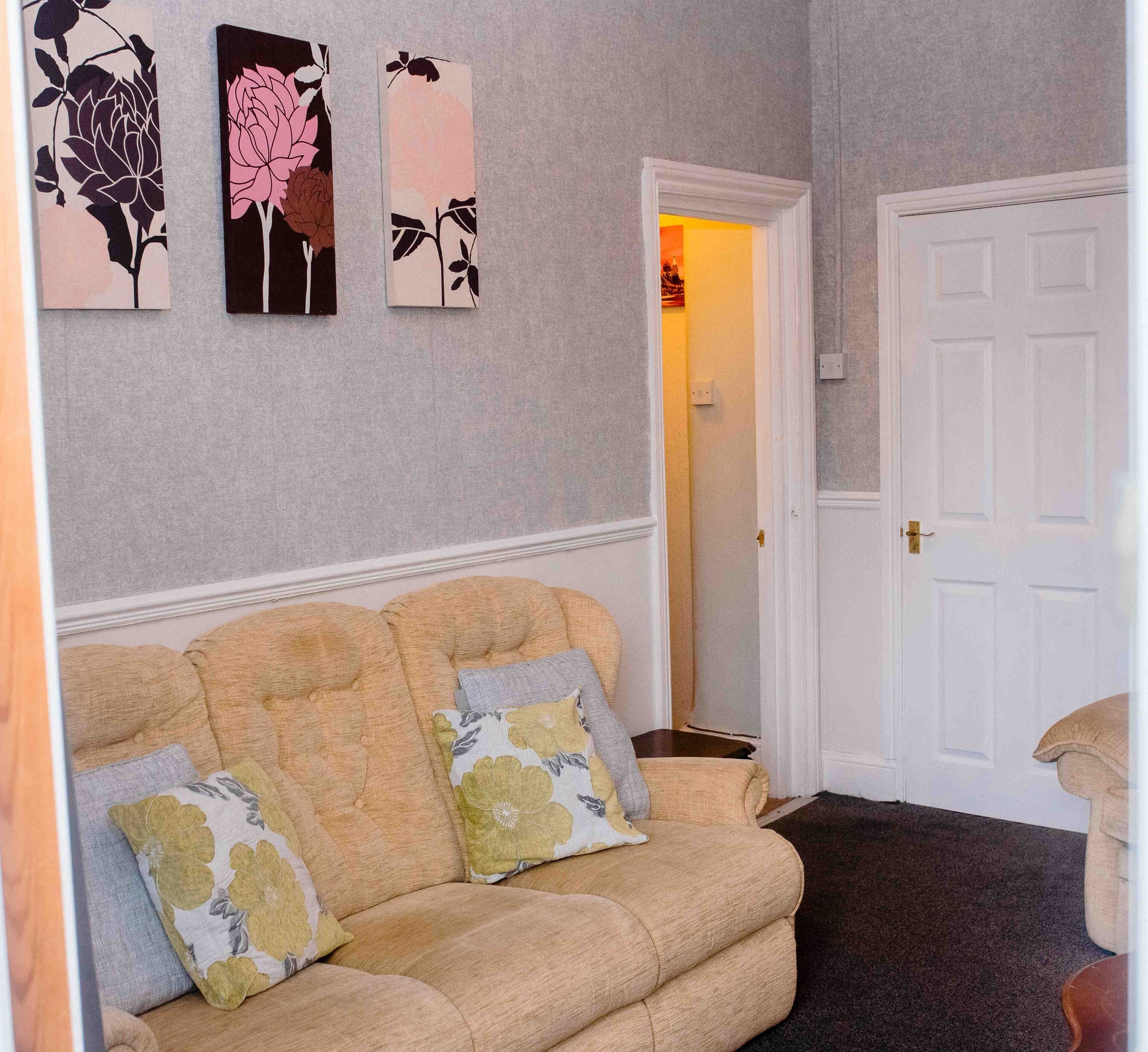 A living room with a beige sofa, two floral cushions, and three wall-mounted floral artworks.