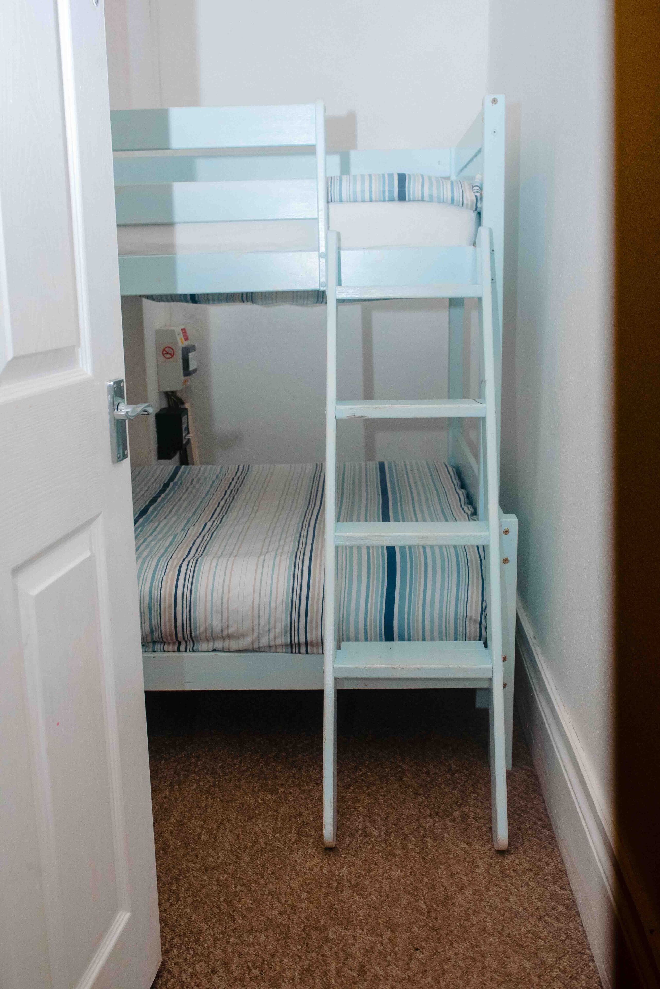 A bunk bed with a striped mattress and a ladder, a door with a handle, and a carpeted floor.