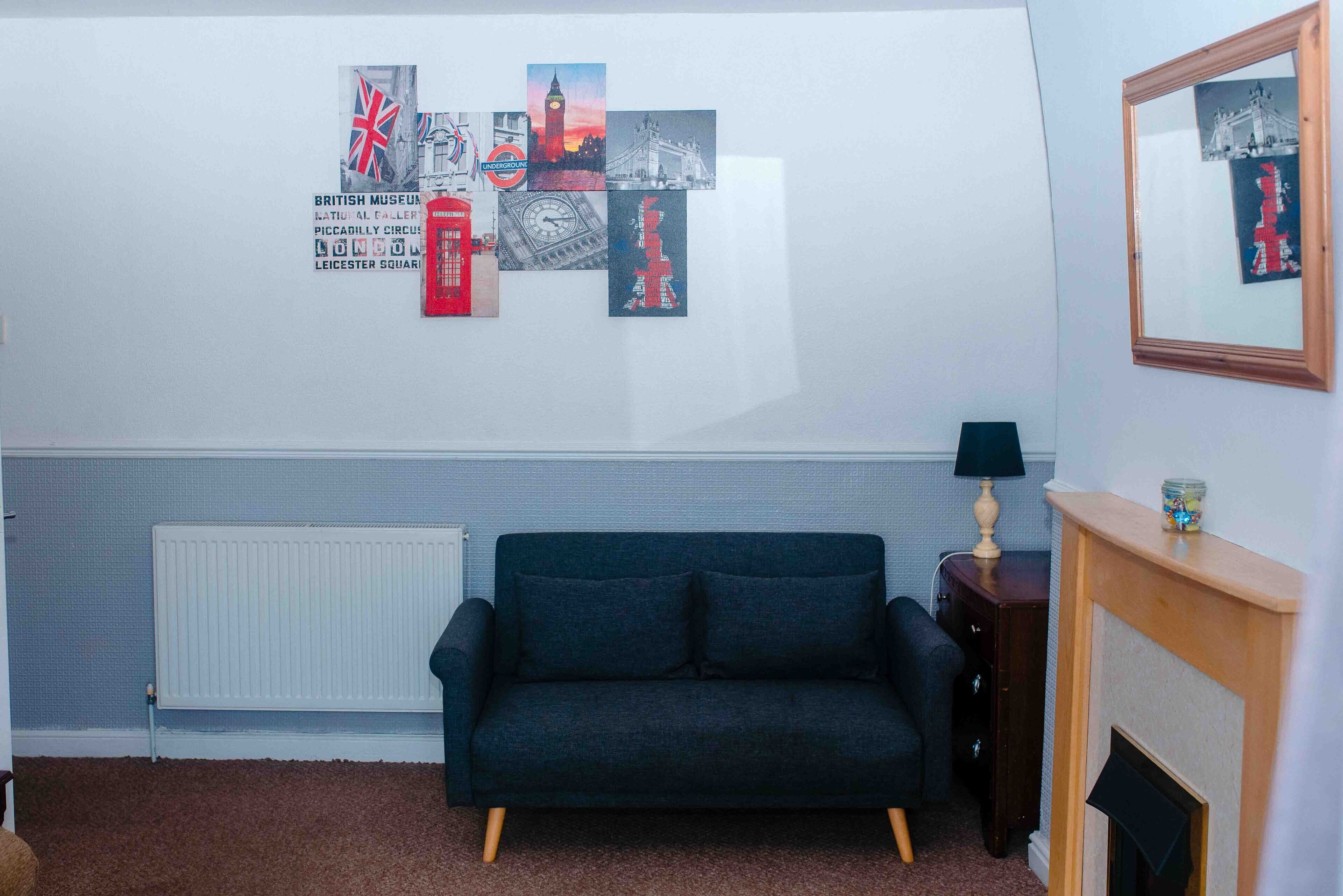 A room with a dark blue sofa, a white radiator, and a wall with various posters.