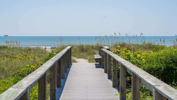 A wooden boardwalk leading to a beach with clear skies and calm waters.