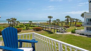 A balcony with a view of the beach, palm trees, and a wooden walkway.