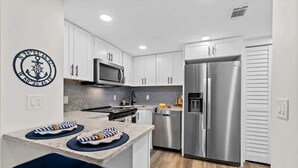 A modern kitchen with white cabinets, stainless steel appliances, and a marble countertop.