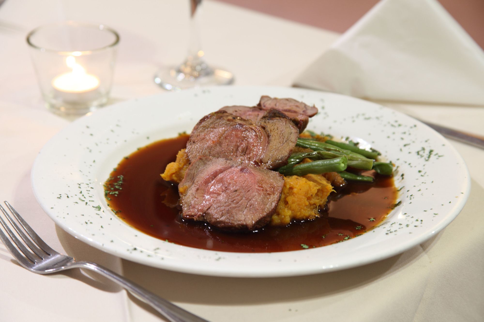 Ein Teller mit Essen, darunter Fleisch, grüne Bohnen und ein gelbes Gemüse, vermutlich Kürbis.