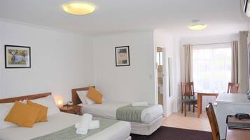A hotel room with two beds, a desk, and a chair. There are two framed pictures on the walls, a window with curtains, and a ceiling light.
