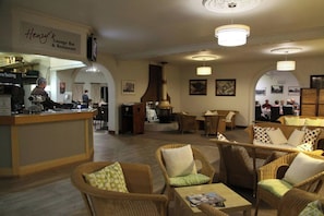 A lounge bar and restaurant with wicker furniture, a bar counter, and a large fireplace. - The Henry Parkes Tenterfield Ex Best Western (Tenterfield)