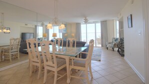 A spacious living area with a glass dining table surrounded by chairs, a sofa, and a television. - Oceanfront 3BR/3BA Crescent Shores North Myrtle Beach (North Myrtle Beach)