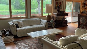 Ein Wohnzimmer mit einer Couch, einem Couchtisch und Blick auf einen Garten durch große Fenster.