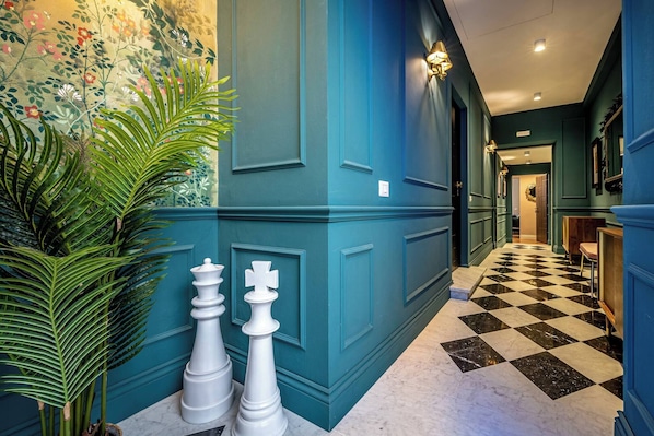 Un couloir aux murs de couleur turquoise, avec un sol à carreaux et des pièces d’échecs.