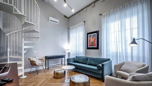 A modern living room with a spiral staircase, a blue sofa, a round coffee table, and a wicker chair. - Hs4U Ricasoli Luxury apartment near Duomo N. 3 (Firenze)