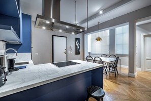 Une cuisine moderne dotée d’un plan de travail en marbre, d’appareils électroménagers en acier inoxydable et d’un coin repas avec un parquet en bois disposé en motif à chevrons.