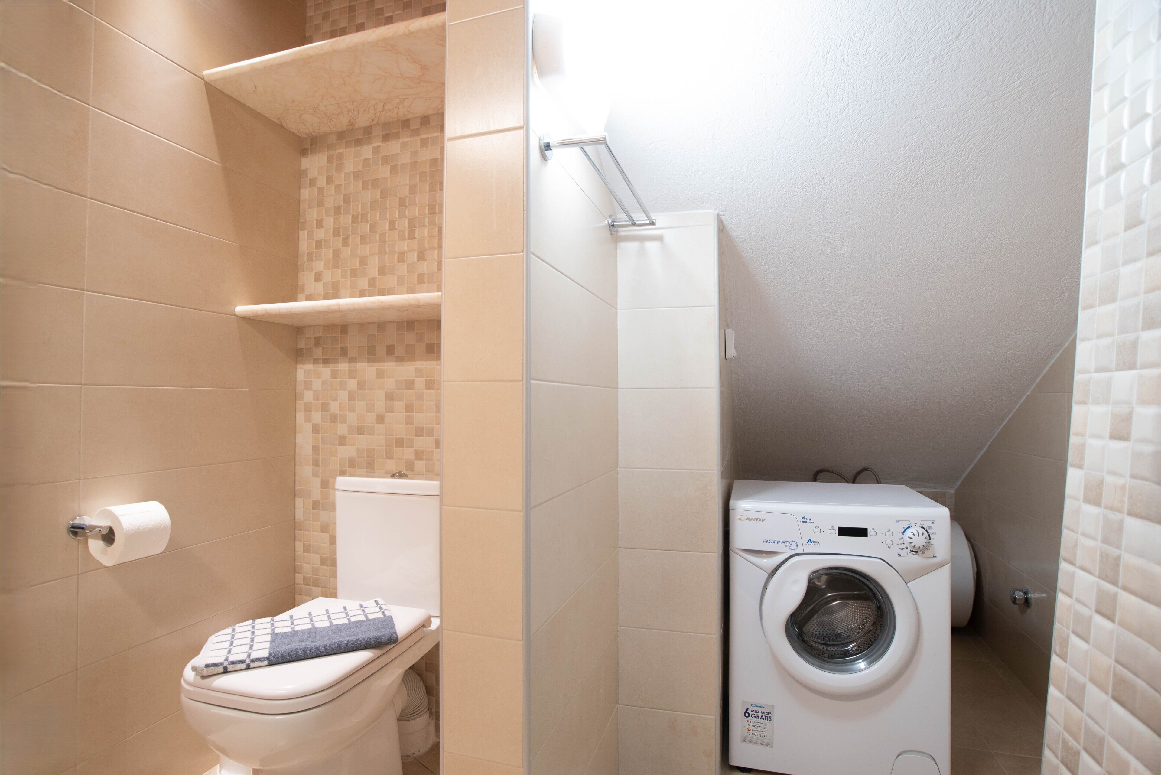 A compact bathroom with a toilet, a washing machine, and a tiled wall.