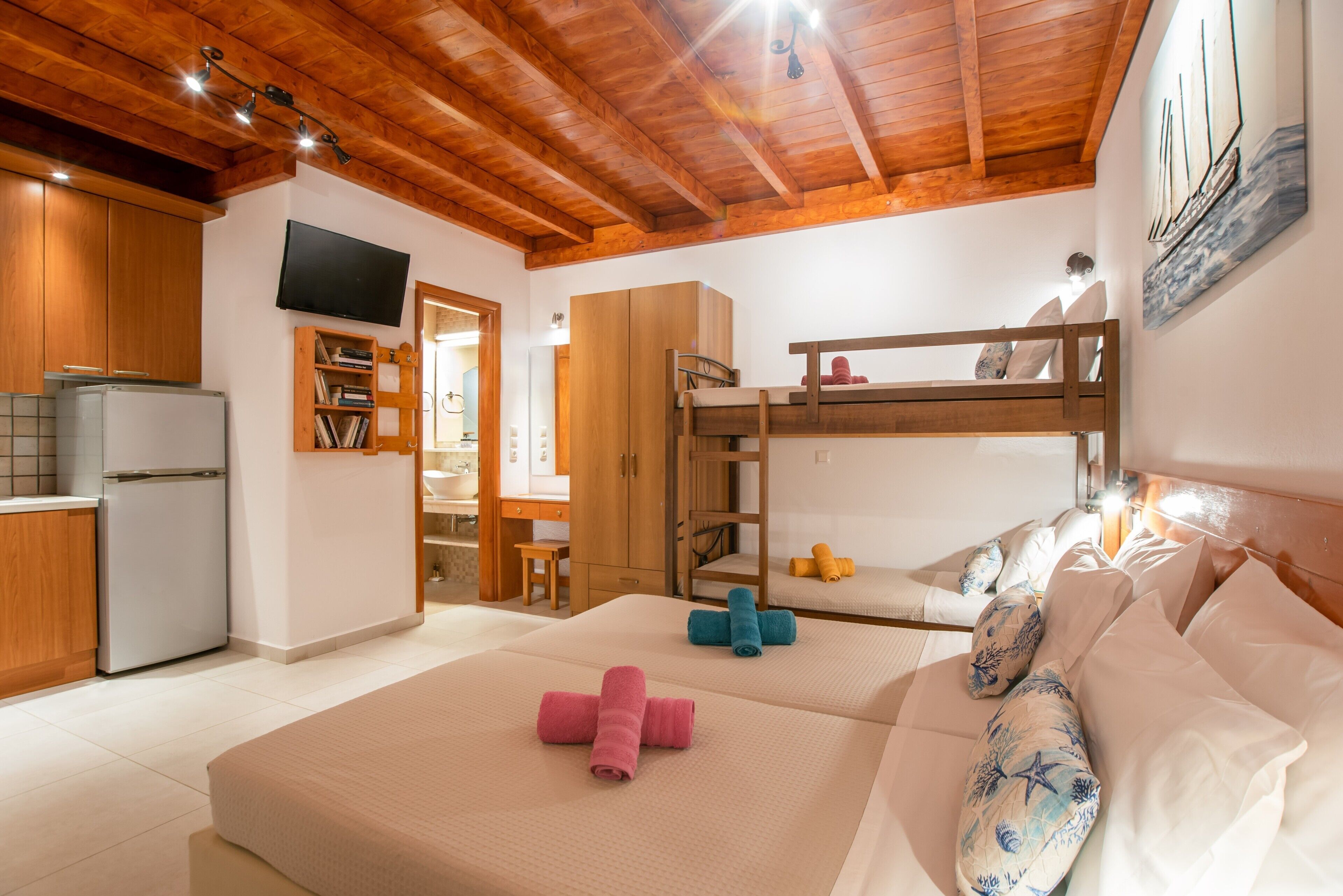 A room with a bunk bed, a kitchen area, and a TV mounted on the wall.