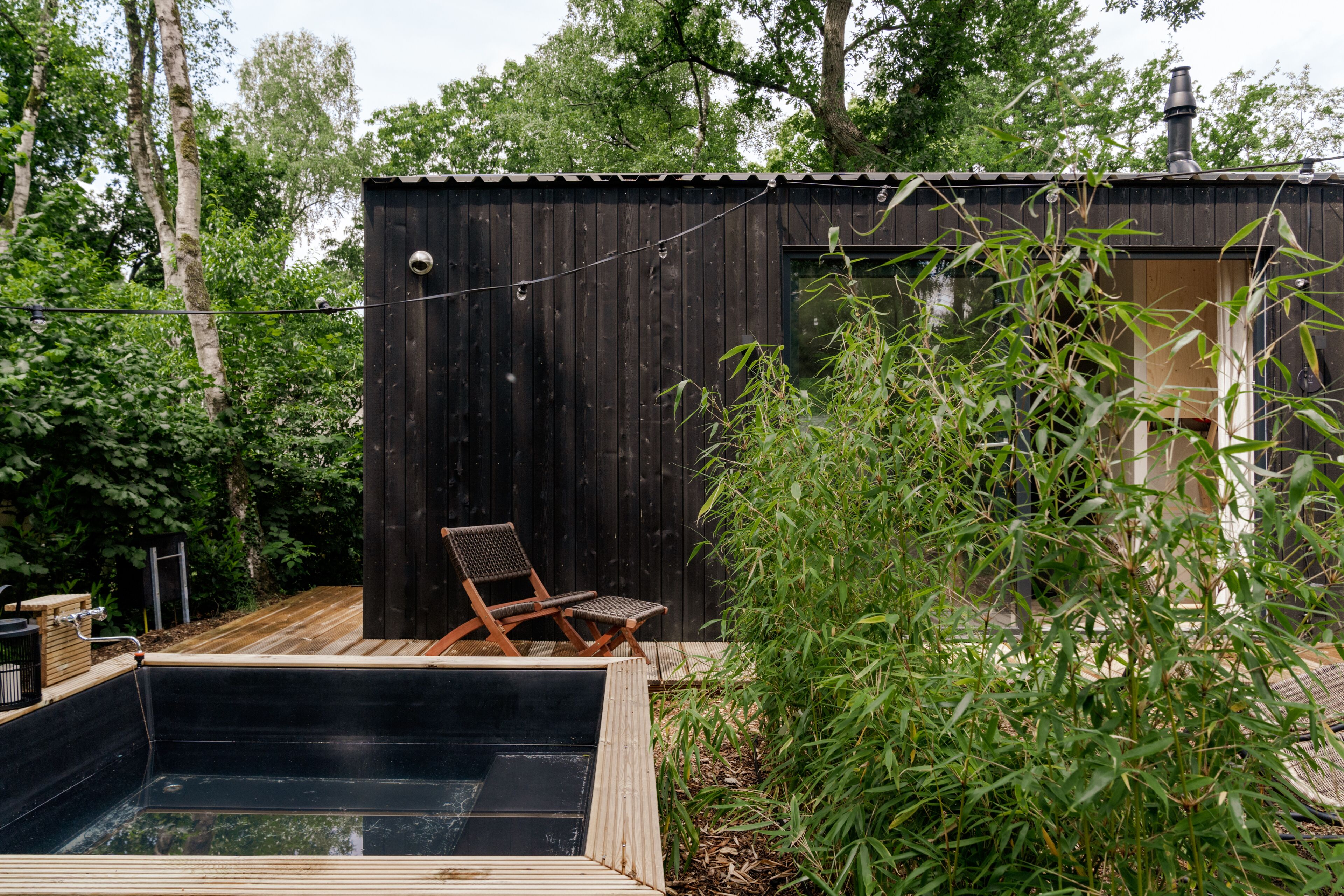 A wooden deck with a hot tub, a wooden chair, and a small shed with a chimney.